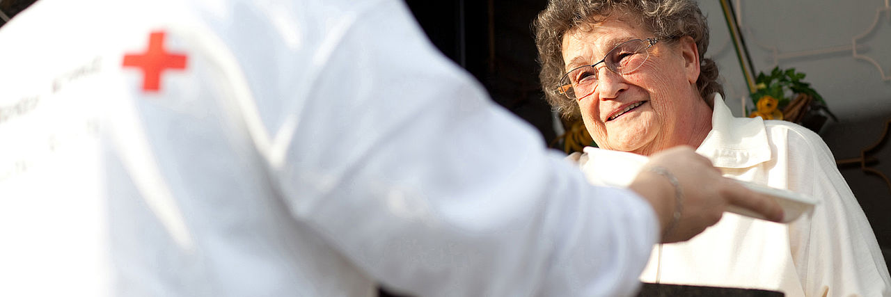 DRK Menüservice Eine Seniorin empfängt ihre Essenslieferung durch einen DRK-Mitarbeiter.